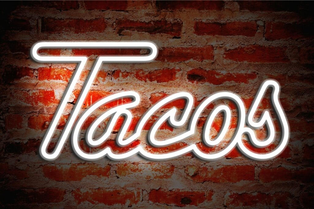 White neon sign that says tacos against a brick wall